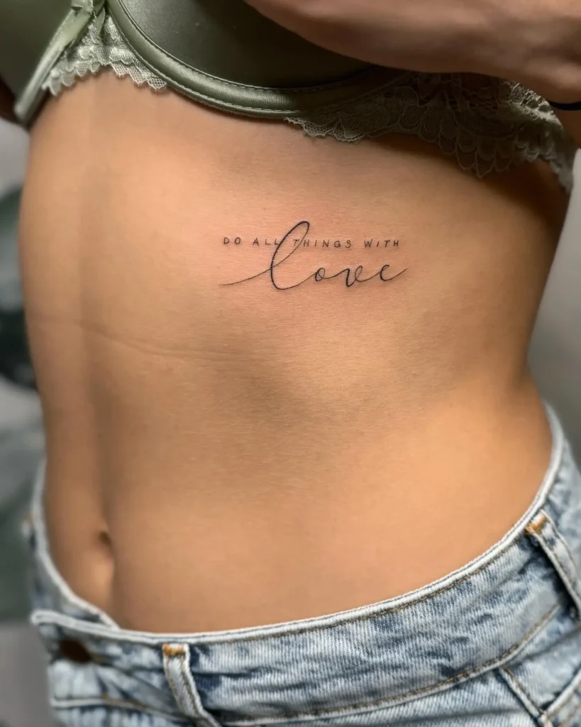 A ribcage tattoo with the phrase “Do all things with love” in delicate script, inspiring kindness, compassion, and mindful living.