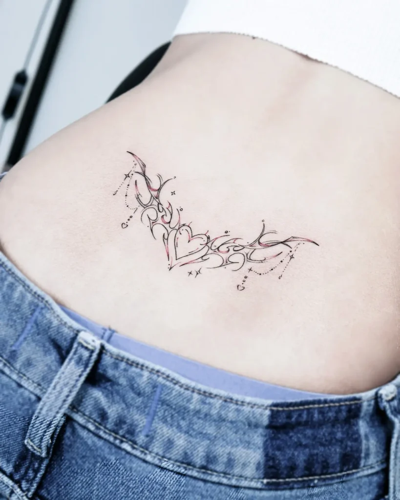 Lower back tattoo with filigree swirls, a central heart, and soft red highlights, accented by tiny stars and dotted lines.