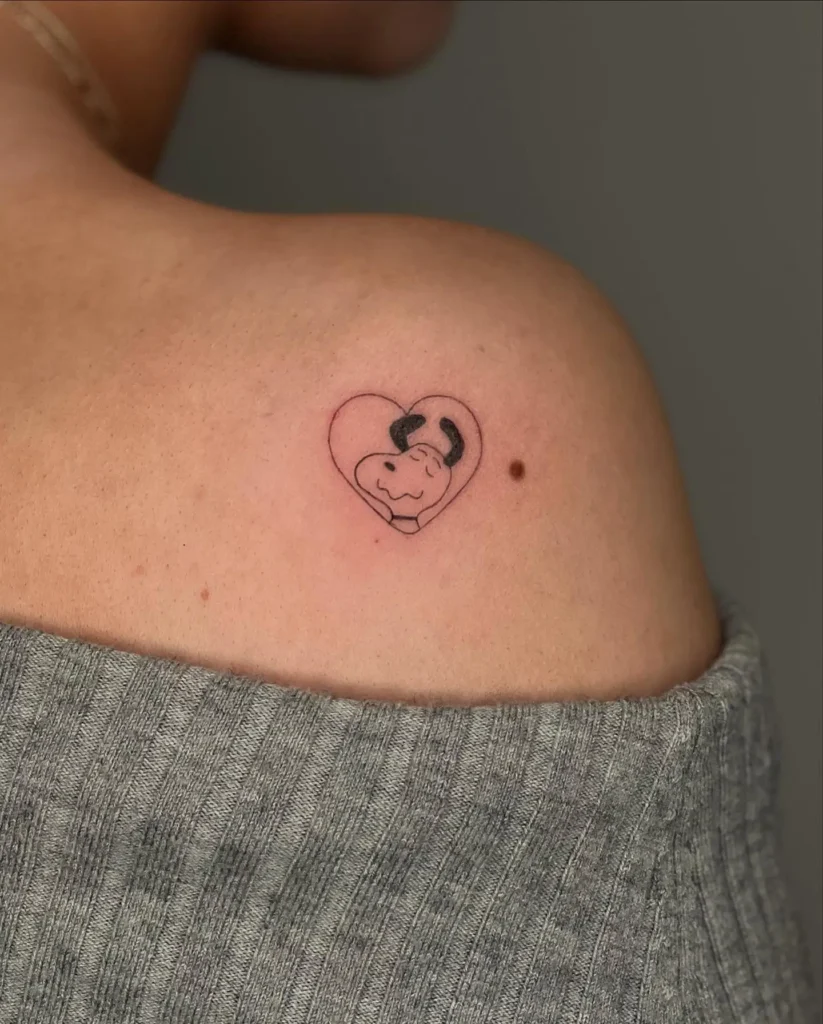 Small shoulder tattoo for women featuring a cute dog face inside a heart outline—minimalist and charming pet-inspired design.