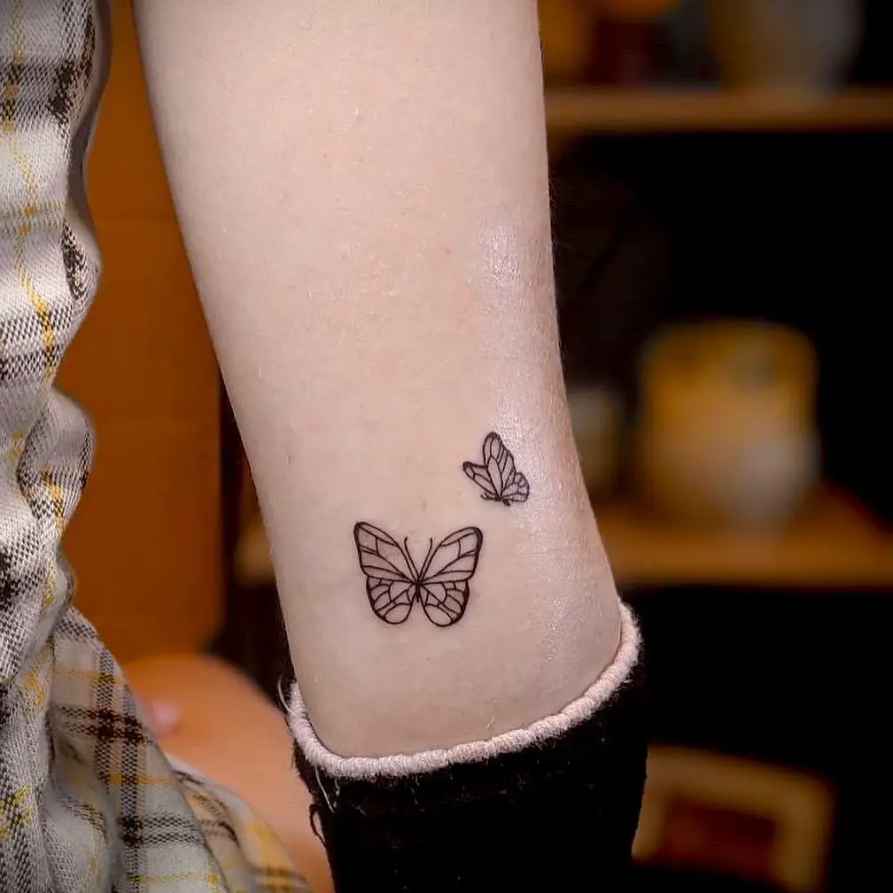 A minimalist ankle tattoo featuring two outlined butterflies, symbolizing growth, transformation, and freedom.