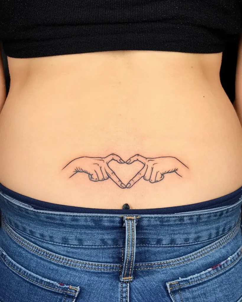Lower back tattoo with two hands outlined in black forming a heart shape.