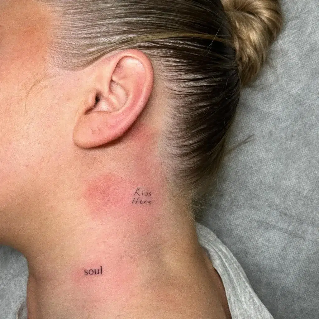
Two small tattoos on the neck: “Kiss Here” in handwritten script behind the ear, and “soul” in lowercase type near the jawline, symbolizing intimacy and self-awareness.