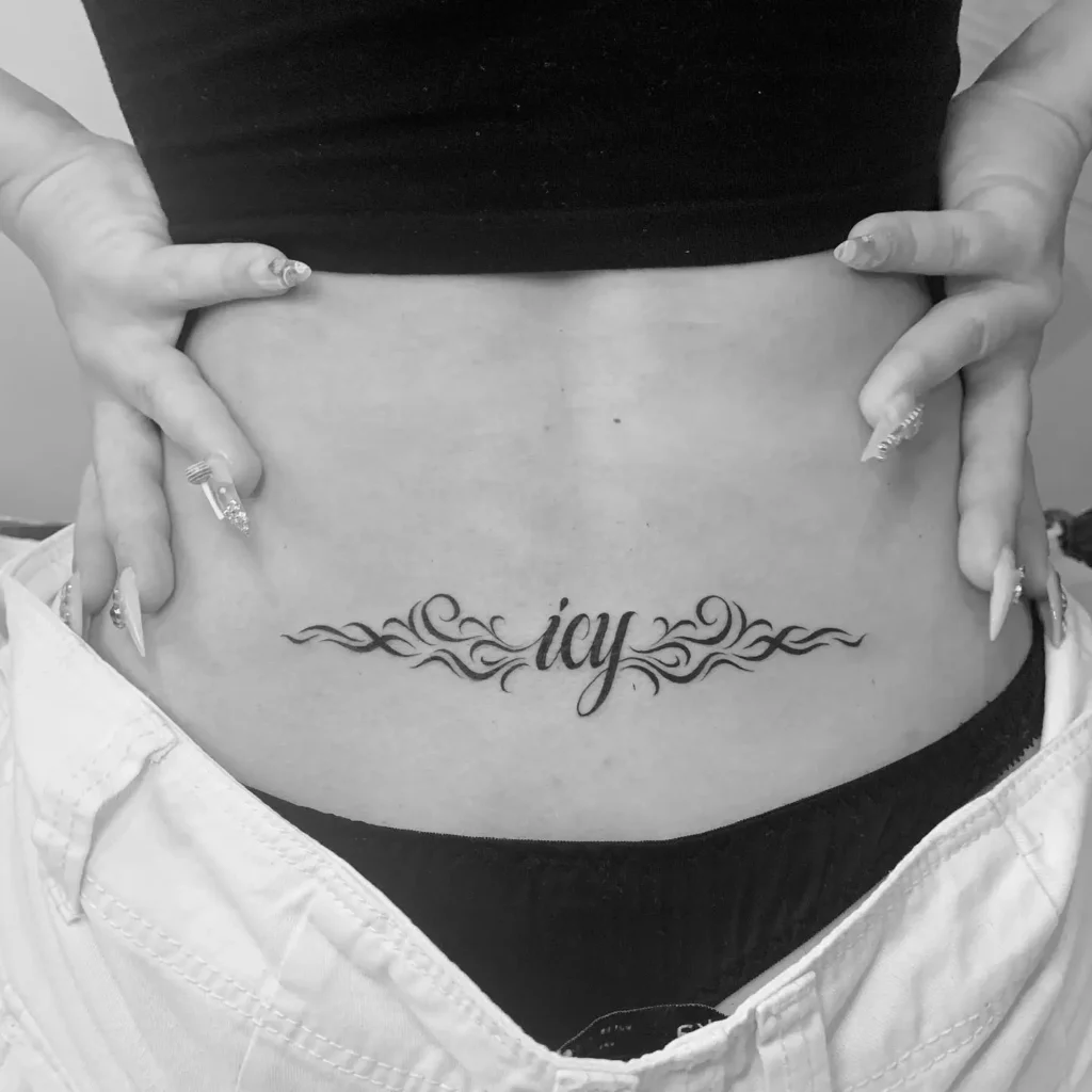 Lower back tattoo featuring the word “icy” in script, framed by tribal swirls in bold black ink.