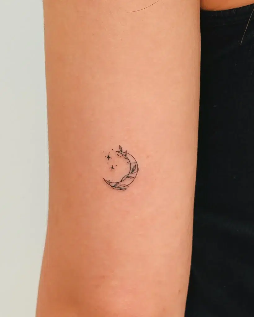 Small crescent moon tattoo for women on the arm, accented with leafy vines and tiny stars—minimalist, botanical, and celestial design.