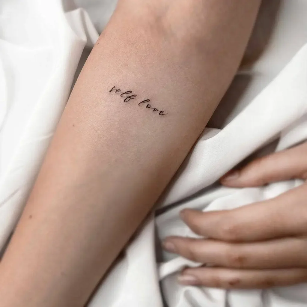 A delicate forearm tattoo in cursive with the words “self love,” symbolizing self-acceptance, growth, and kindness.