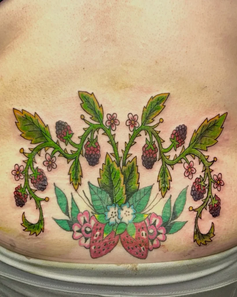 Lower back tattoo with colorful strawberries, blackberries, green leaves, and pink flowers in a botanical arrangement.