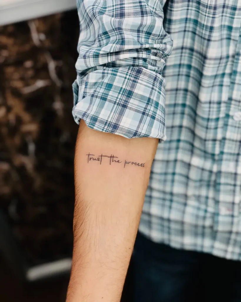 A forearm tattoo in fine script that reads “trust the process,” symbolizing patience, faith, and personal growth.