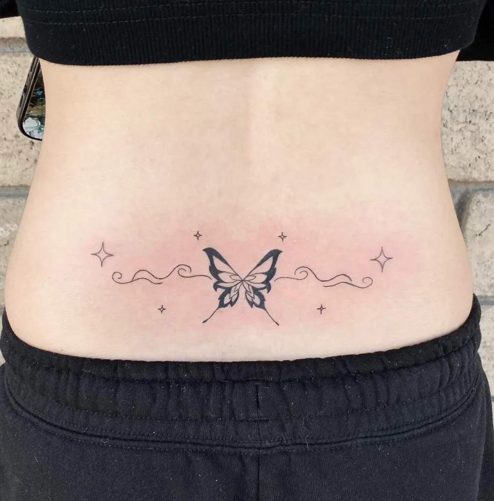 Lower back tattoo featuring a minimalist butterfly with wavy lines and small star accents in fine black ink.