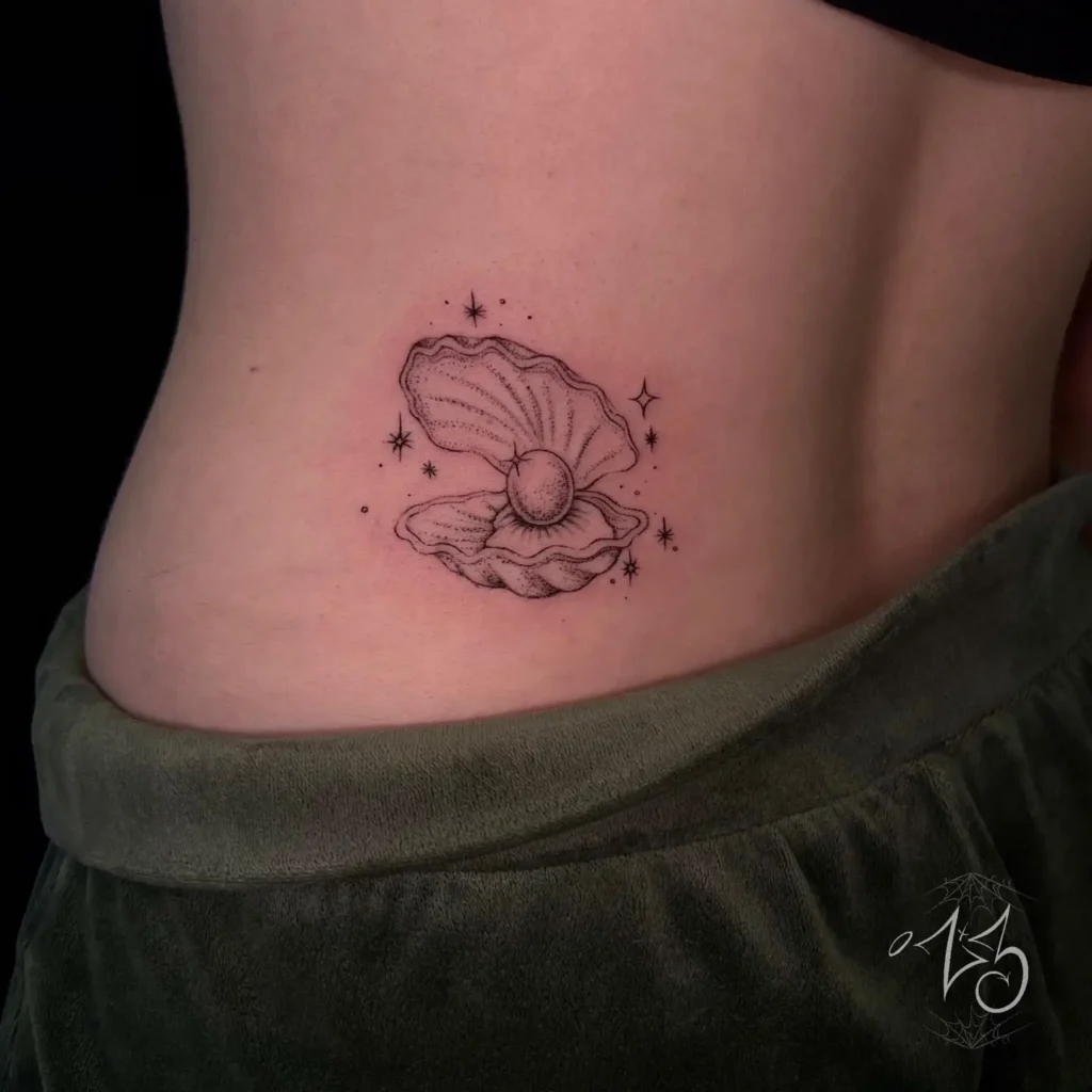  Lower back tattoo of an open oyster shell with a pearl inside, surrounded by dotted stars and sparkles.