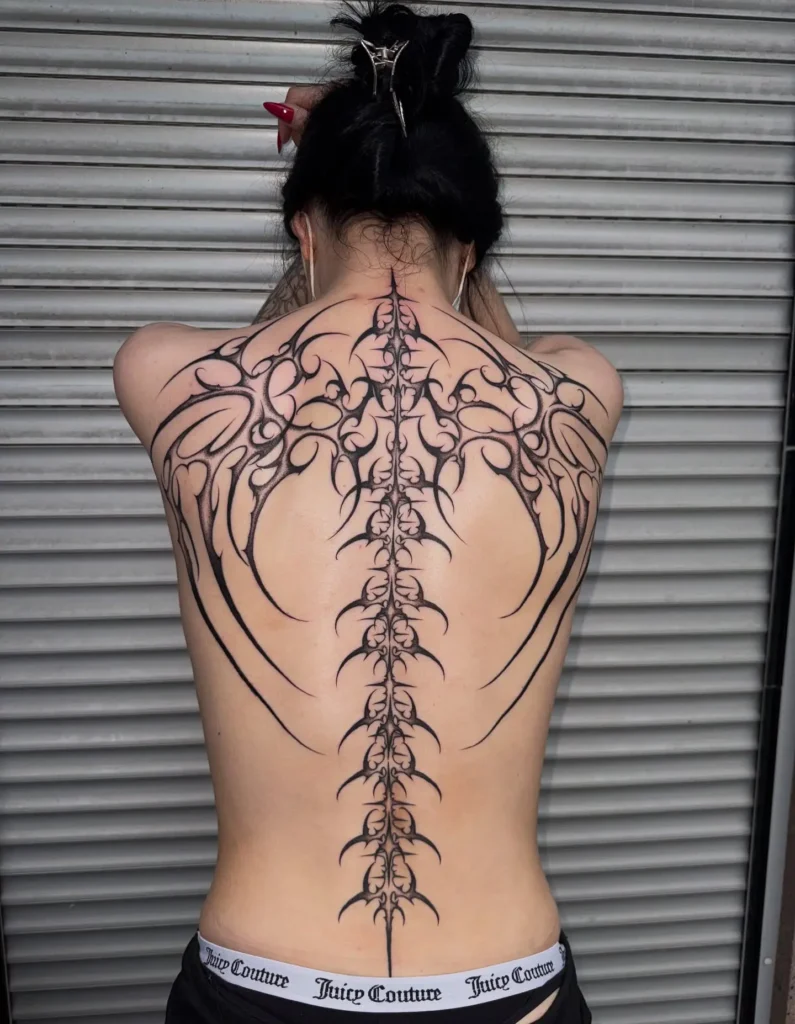 Full back tattoo featuring bold tribal patterns running along the spine with wing-like extensions across the back and lower back.