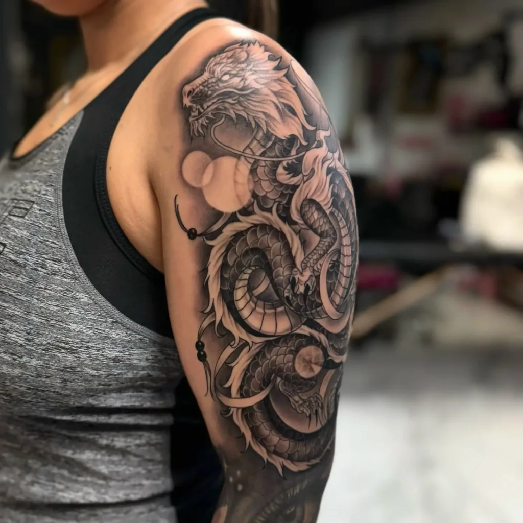 Black and gray sleeve tattoo on a woman’s arm featuring a detailed dragon with scales, whiskers, claws, smoke, and mystical orbs.