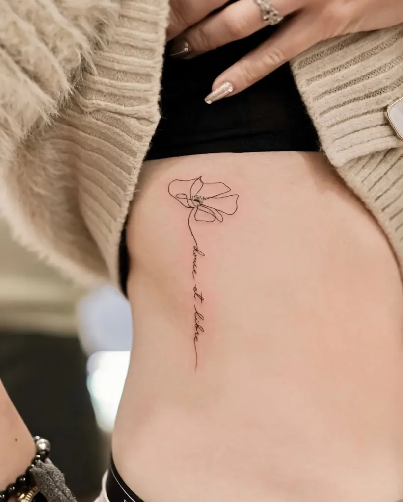 Minimalist one-line poppy tattoo with French script "douce et libre" on ribcage, symbolizing freedom and personal strength through fineline floral ink.