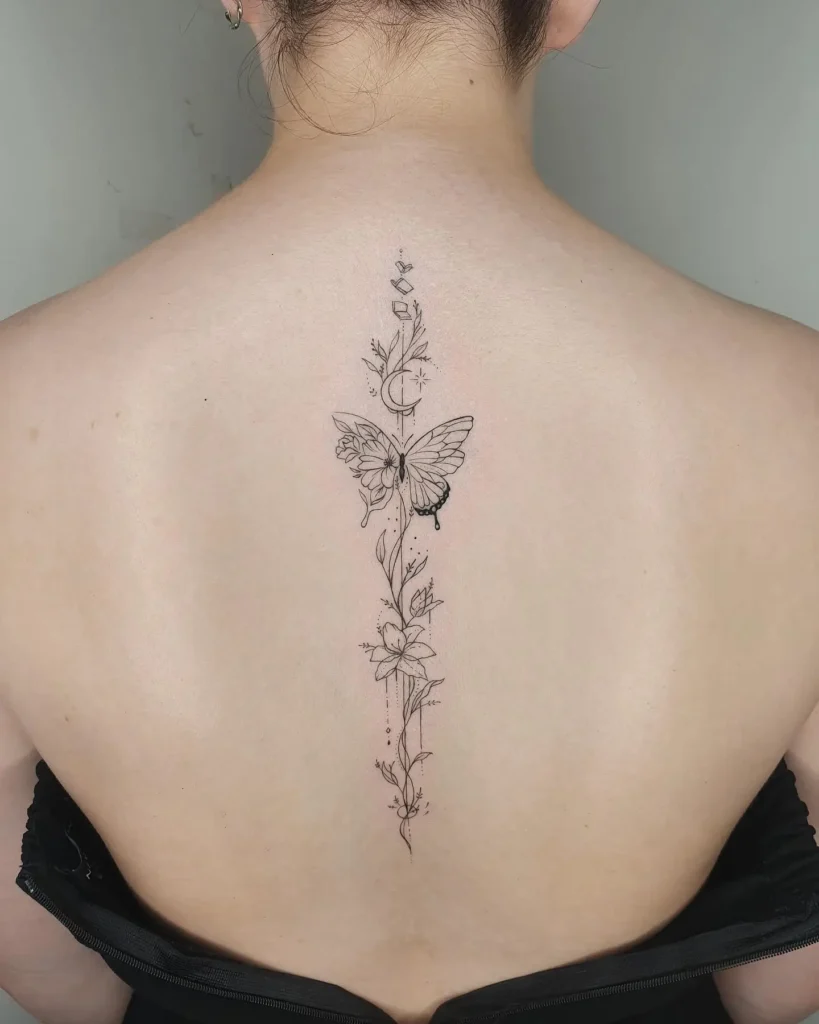 A fine-line butterfly and floral spine tattoo with celestial accents on a woman’s back.