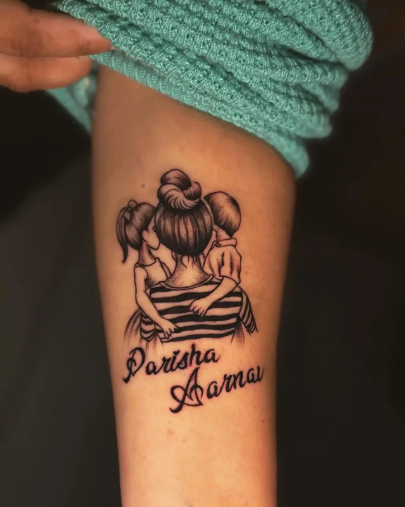 Black and grey tattoo shows a mother with her hair in a bun, hugging her daughter and son closely from behind. The mother wears a striped shirt, and both children lean into her embrace. Below the family scene, the names “Parisha” and “Aarnav” are written in elegant script. The tattoo celebrates mom and daughter tattoos unique, family bonds, and love.