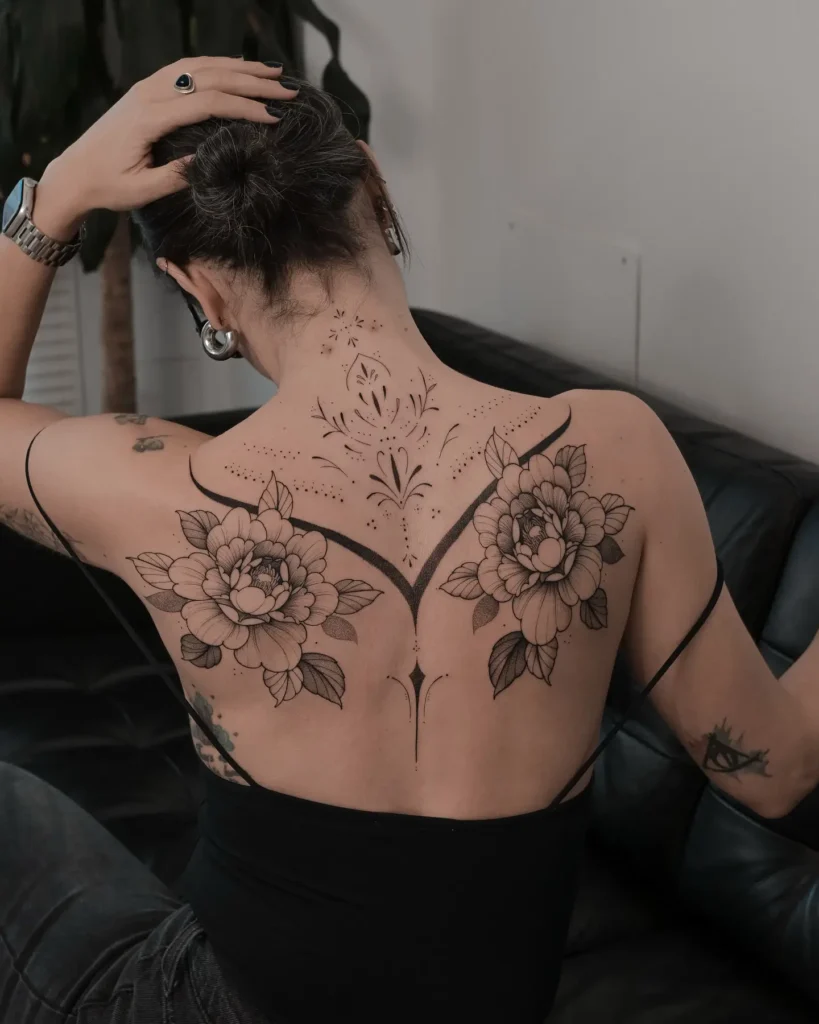 Symmetrical peony floral back tattoo for women featuring bold outlines and ornamental spine design, representing elegance and harmony

