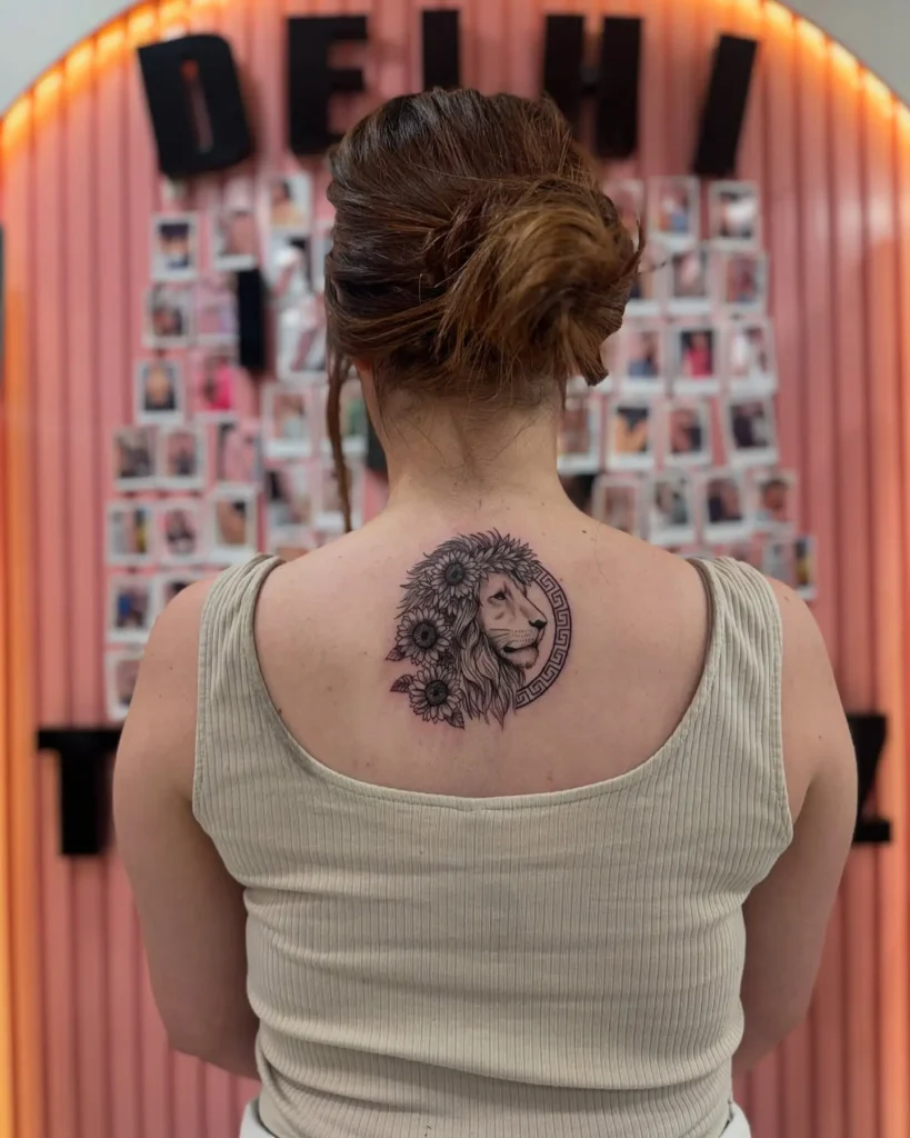 Detailed lion tattoo on upper back, framed with sunflowers and bordered with Greek pattern. Tattoo blends bold lines and floral softness, creating a fierce yet peaceful look. Suitable for animal tattoo ideas back or sleeve placements. Strong visual for those exploring animal tattoo ideas simple yet striking in meaning.