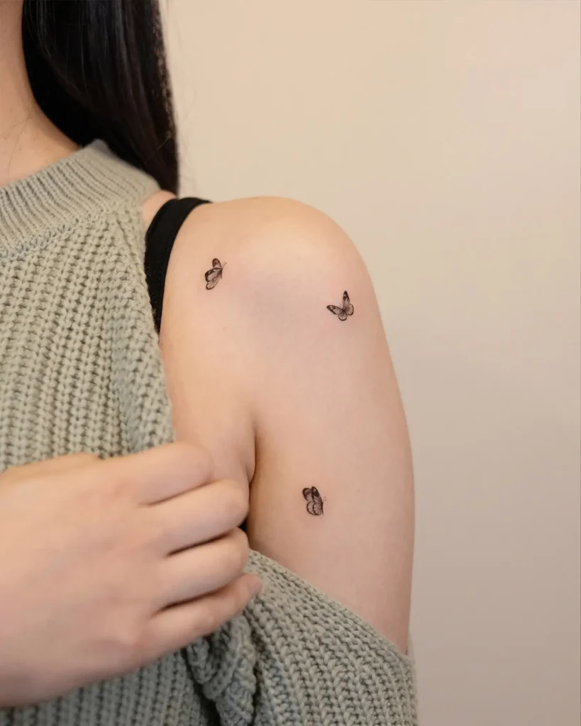 Three small black butterfly tattoos inked on the shoulder and upper arm of a woman.