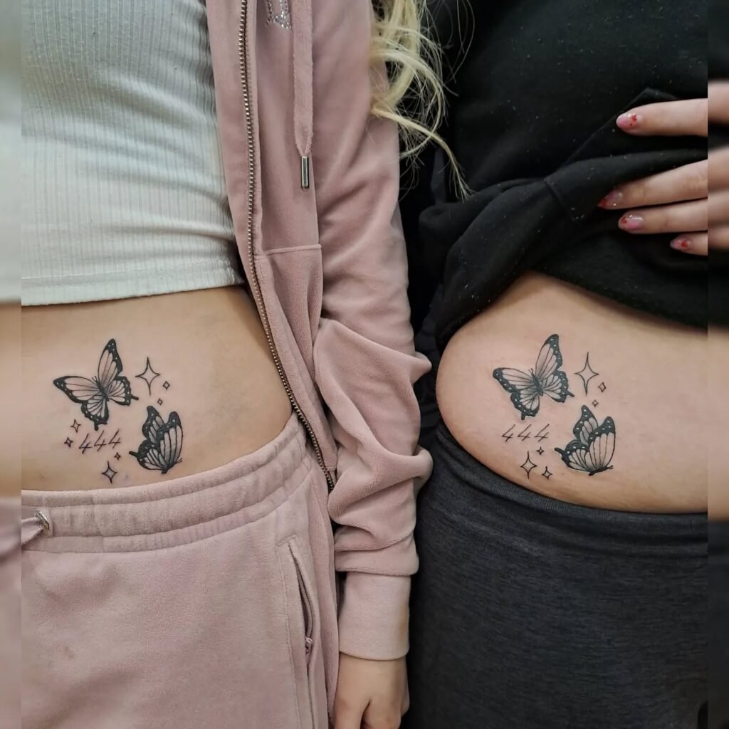 Matching tattoos on two women’s hips, each showing two shaded butterflies surrounded by small sparkles and the number 444 in fine script. The butterflies have detailed wings, and the overall design uses black ink for contrast. This tattoo captures mom and daughter tattoos butterfly style, representing unity, protection, and shared journeys through life.