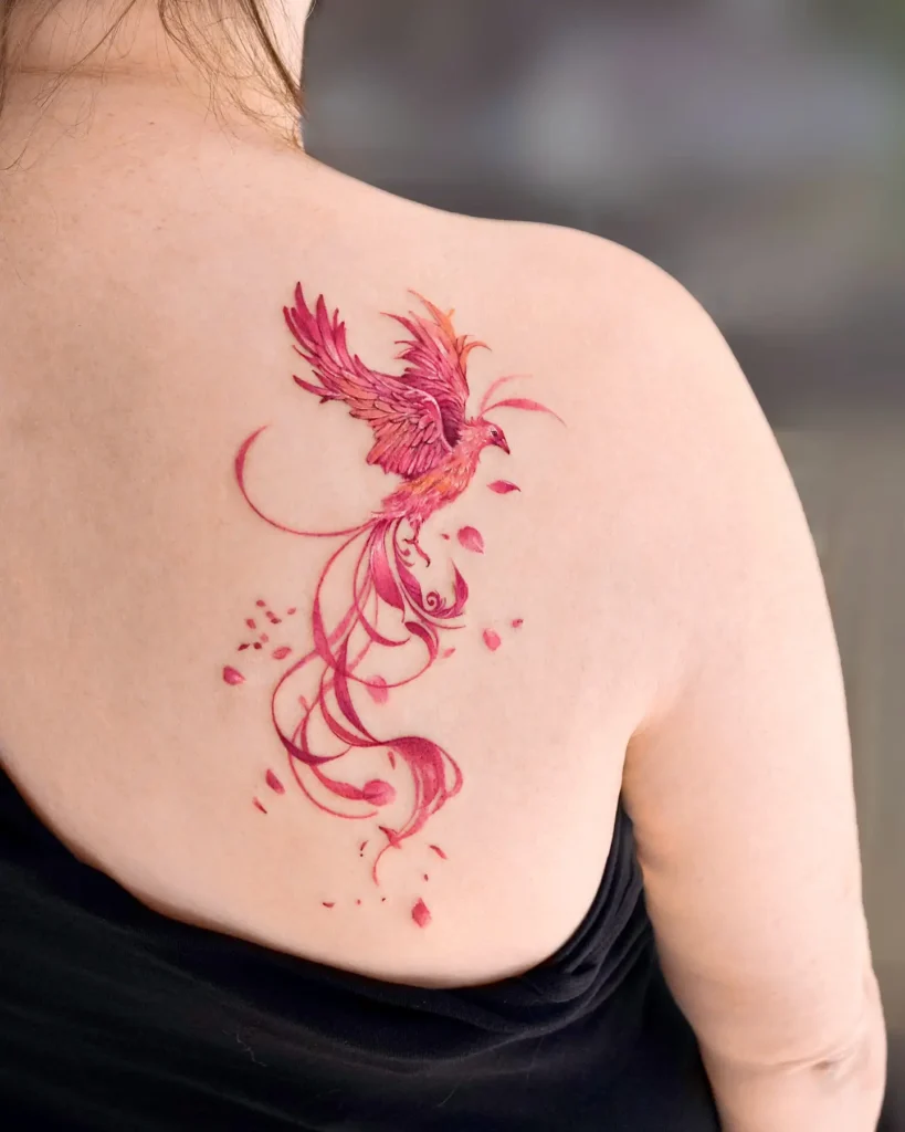 Colorful watercolor phoenix tattoo on woman’s back, symbolizing transformation, passion, and artistic rebirth