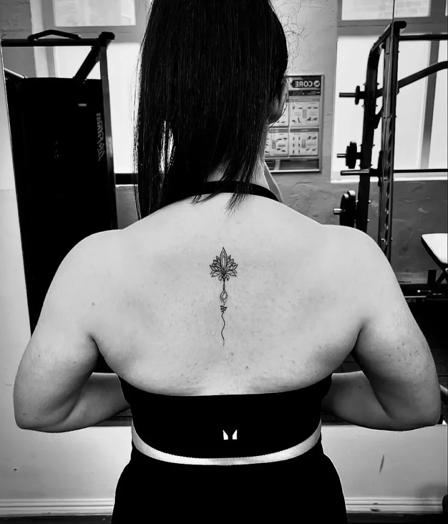 Delicate ornamental tattoo with floral elements running vertically along the upper spine of a woman’s back.