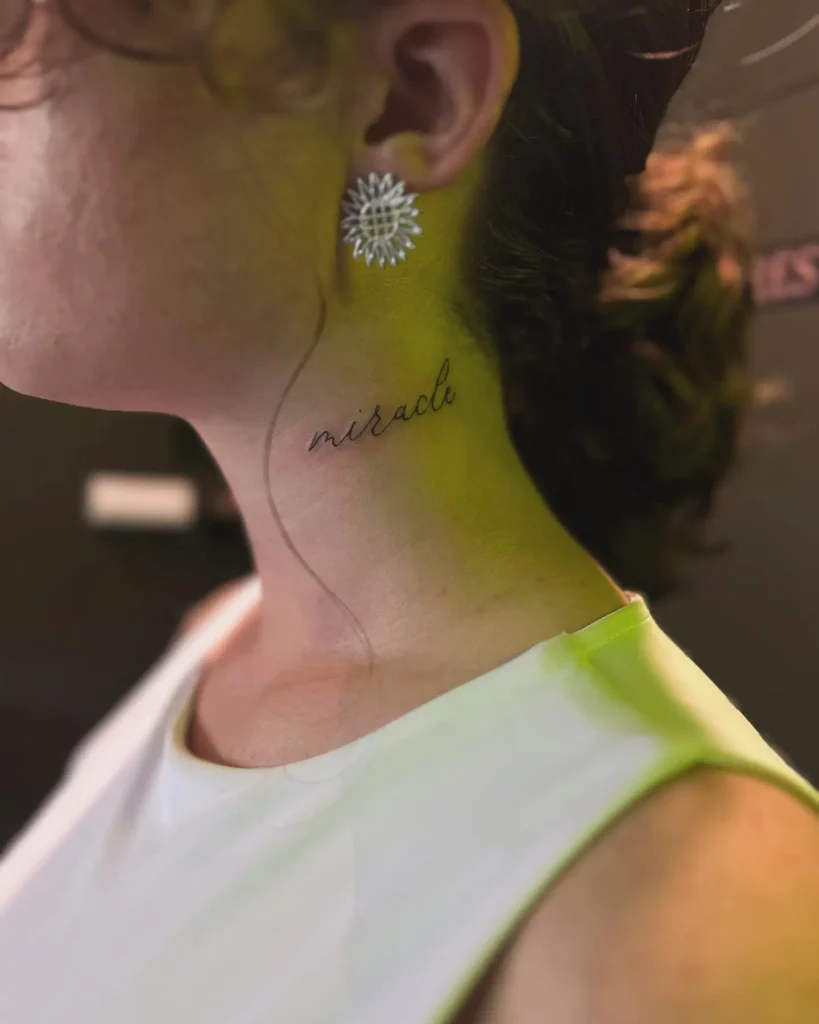 Small script neck tattoo for women reading “miracle,” placed along the throat in fine black cursive lettering.