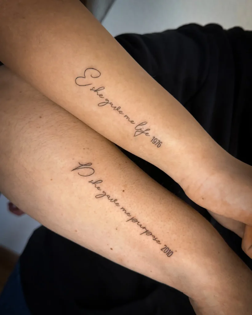 Matching forearm tattoos in elegant script, one reading “She gave me life 1976” and the other “She gave me purpose 2010.” The minimal black ink handwriting style honors the special connection between a mother and daughter, highlighting birth and purpose in a deeply personal way.