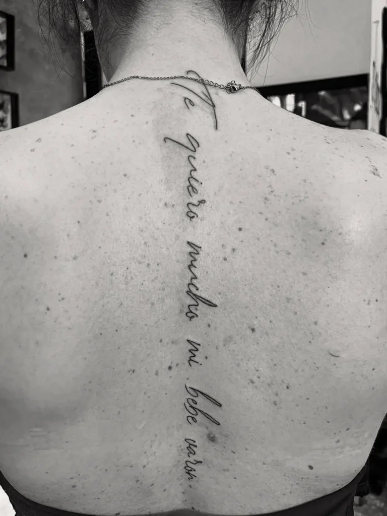 A Spanish quote spine tattoo in elegant script lettering running vertically down a woman’s back.