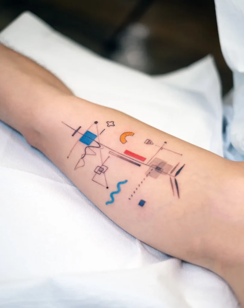 Abstract geometric tattoo on arm with colorful shapes including squares, lines, curves, and a crescent moon in blue, red, orange, and black tones.