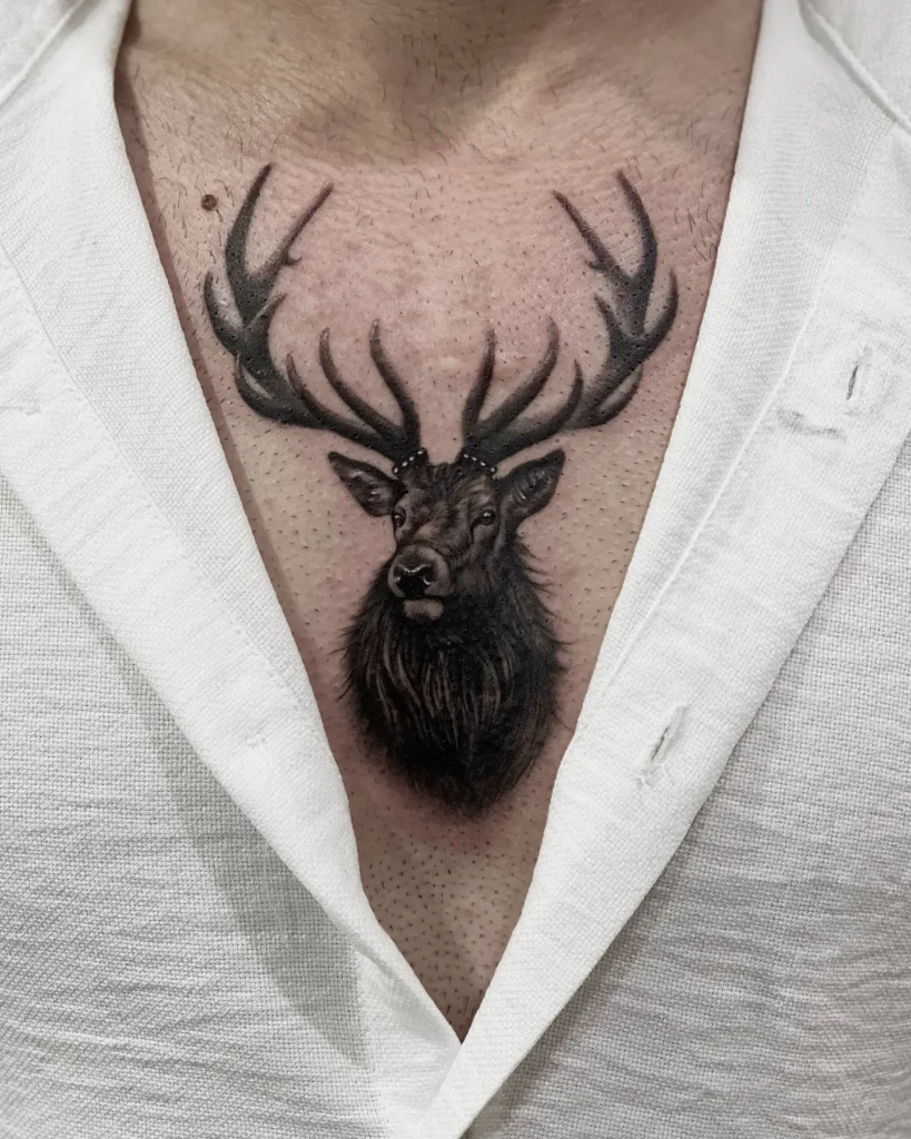 Detailed black and grey chest tattoo of a realistic stag with antlers reaching across the collarbones. Placed in the center of the chest for symmetry and impact. Fine shading enhances texture in fur and antlers, creating a powerful and majestic wildlife design.