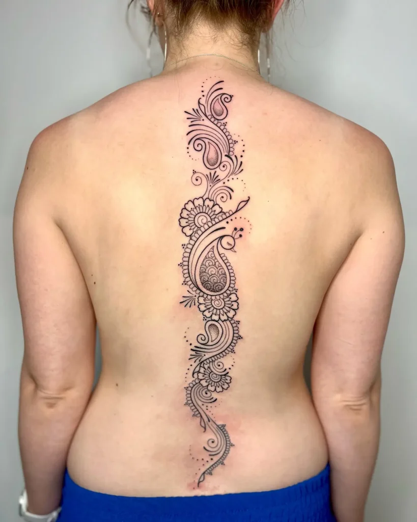 A paisley-inspired spine tattoo with swirling lines, dotted accents, and floral details running down a woman’s back.