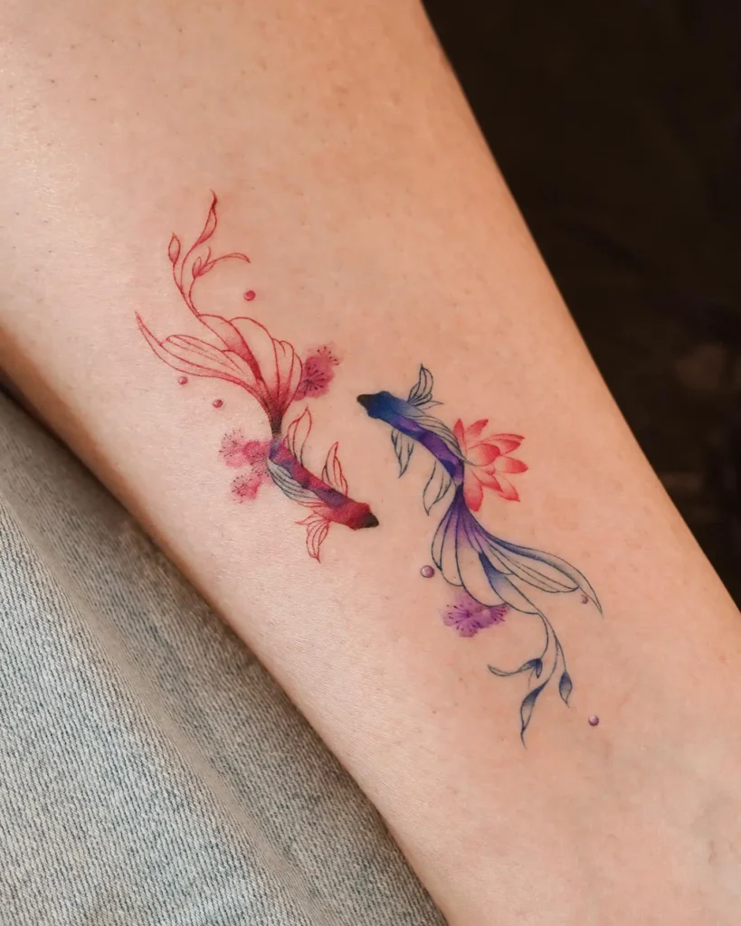 Watercolor tattoo of two koi fish on the leg, one in red with pink blossoms and one in blue-violet with lotus petals. The design flows with delicate floral extensions from the fins, evoking motion and balance. Positioned to mirror each other, this tattoo symbolizes duality, peace, and natural beauty.