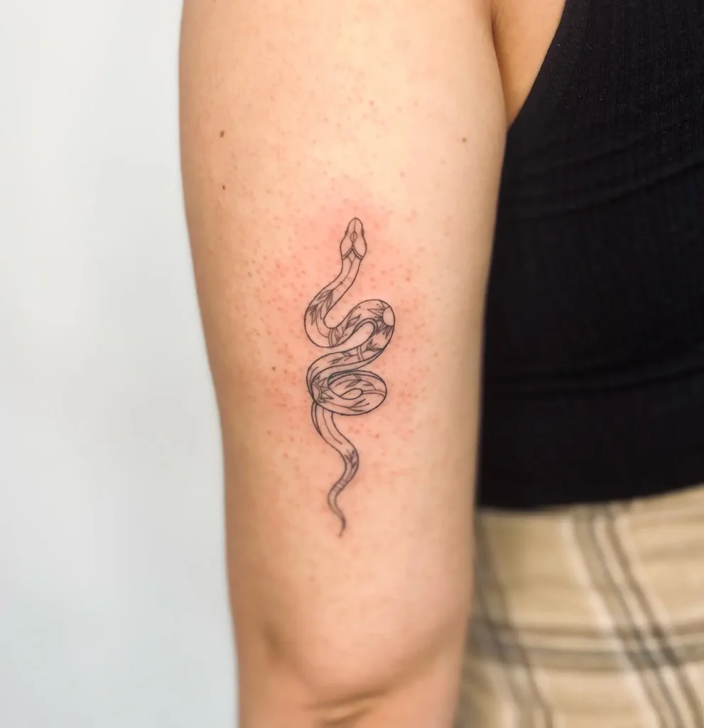 Fine line floral snake tattoo on upper arm with minimalistic design and soft inner detailing.