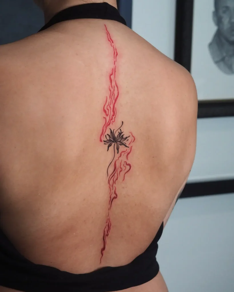 A spine tattoo with red flame-like lines and a central black abstract flower running vertically down a woman’s back.
