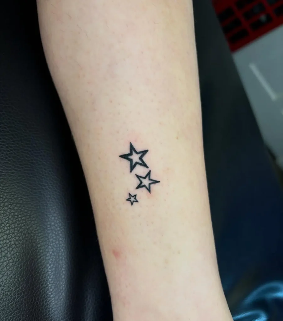 Three bold black outlined star tattoos in a row on a woman’s forearm, each a different size.