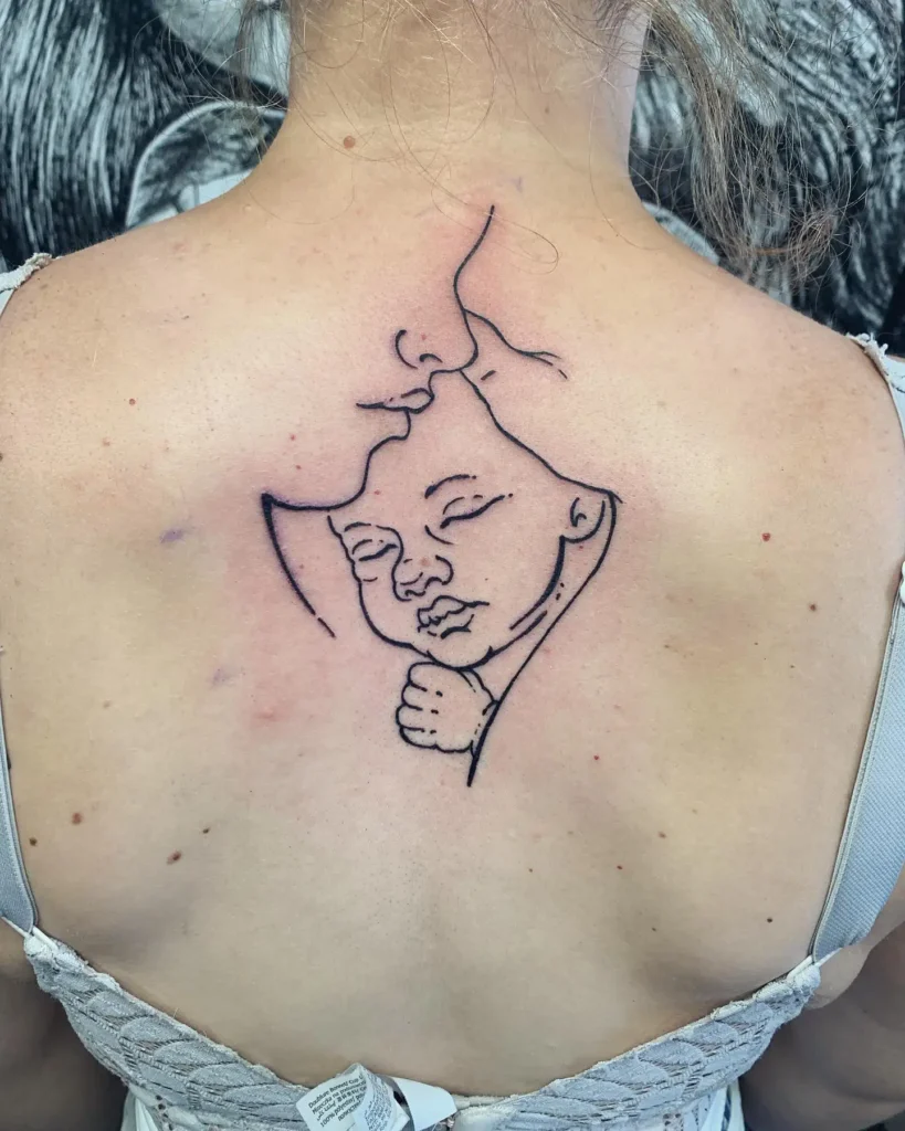 Back tattoo shows a minimalistic, continuous line drawing of a mother tenderly kissing her baby’s forehead. The child’s eyes are closed, and the overall look is peaceful and comforting. Clean black ink lines form the entire image, creating a special piece for mom and daughter tattoos unique, honoring love, nurture, and quiet connection.