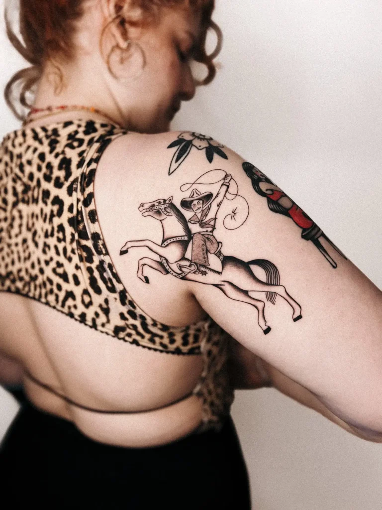 Cowgirl riding a horse tattoo on shoulder in vintage style, detailed line work suited for animal tattoo ideas arm or Americana themes.


