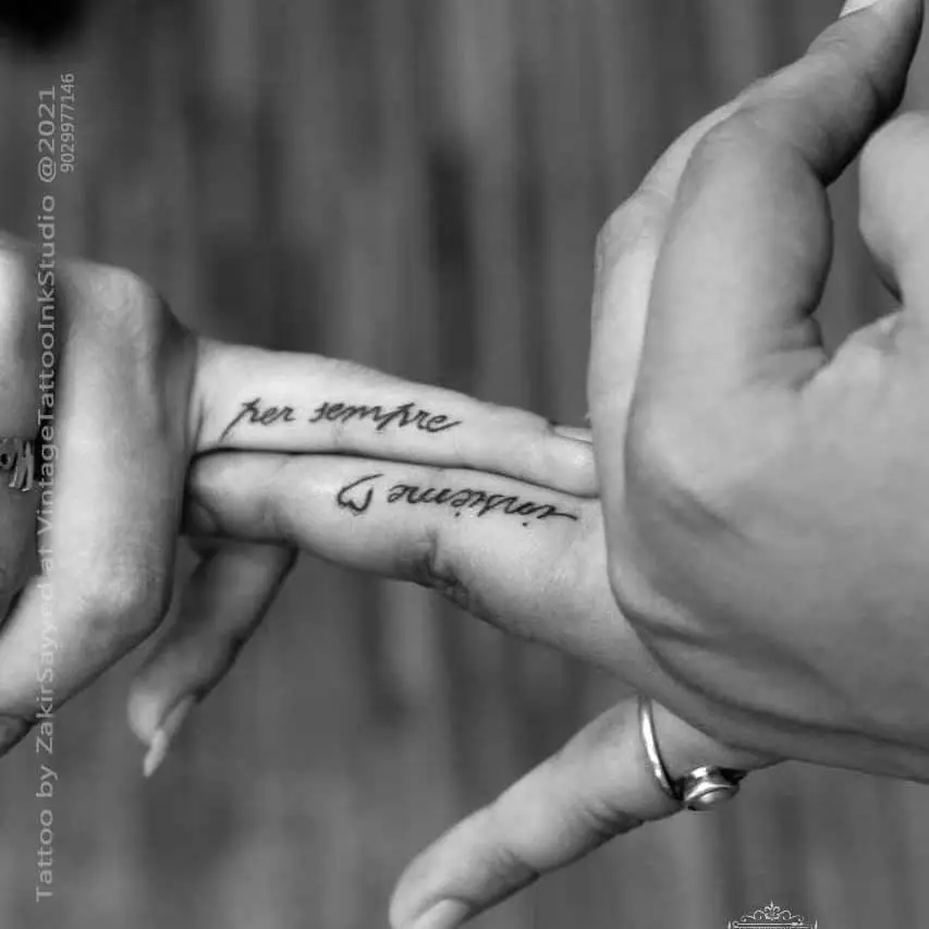 Black and white photo showing a couple's matching finger tattoos. The phrase “per sempre” (forever) is inked in elegant cursive script on one partner's finger, while “insieme” (together) appears on the other, forming the message “forever together” when fingers are placed side by side. A small heart connects the two. This romantic tattoo concept is ideal for couples seeking symbolic and intimate finger tattoo designs.










