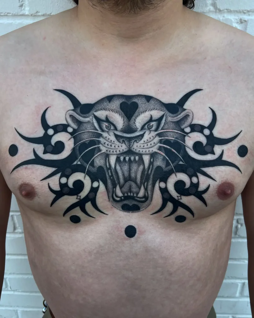 Chest tattoo for men featuring a roaring panther head in the center, framed by symmetrical tribal blackwork and dot-shaded detailing; powerful and aggressive design representing courage and dominance.