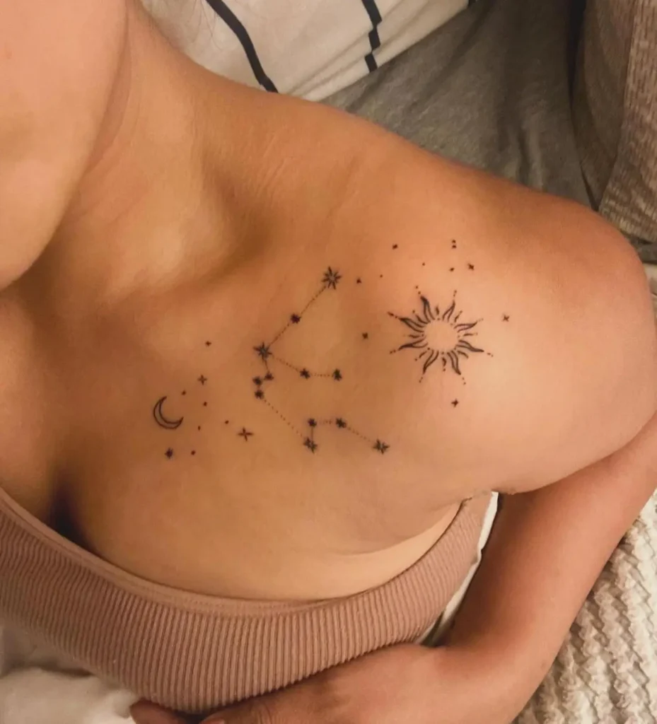 Celestial tattoo on a woman’s collarbone, showing a crescent moon, stars, a sun, and constellation details.