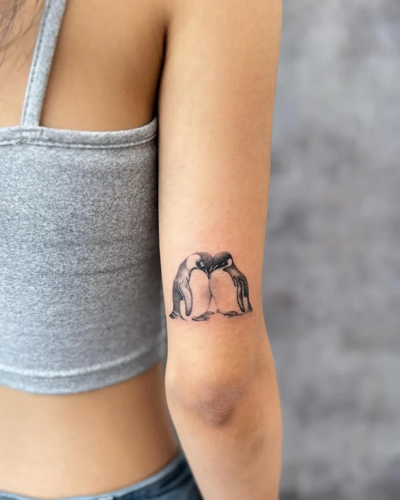 Realistic penguin tattoo showing two penguins forming a heart shape, symbolizing love and bond, great for animal tattoo ideas arm or sleeve.

