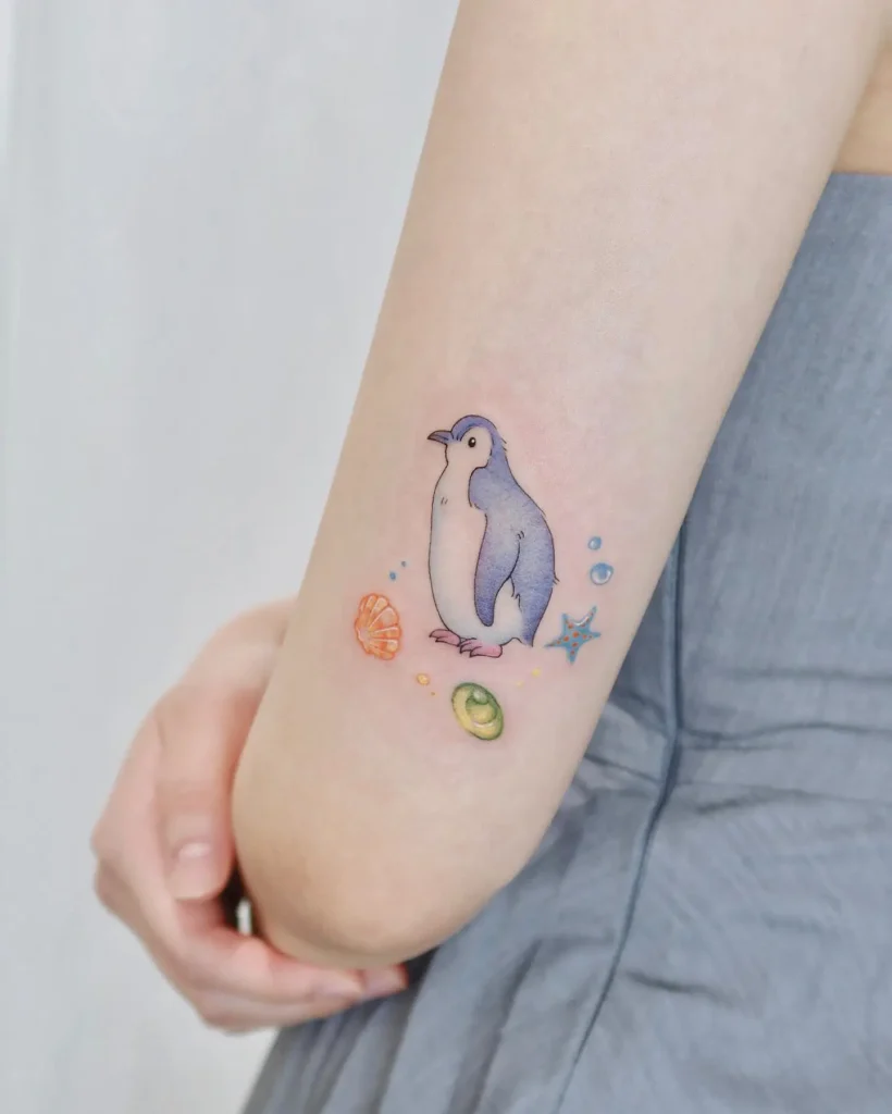 Cute watercolor penguin tattoo with seashells and bubbles on arm, soft colors perfect for animal tattoo ideas easy or sleeve inspiration.

