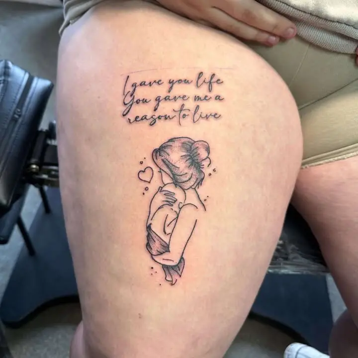 Thigh tattoo features a minimalist drawing of a mother holding her daughter close, with hearts nearby. Above the figures, script text reads “I gave you life. You gave me a reason to live.” The black ink and fine lines highlight the emotional connection, making this a meaningful choice for mom and daughter tattoos focused on love and gratitude.
