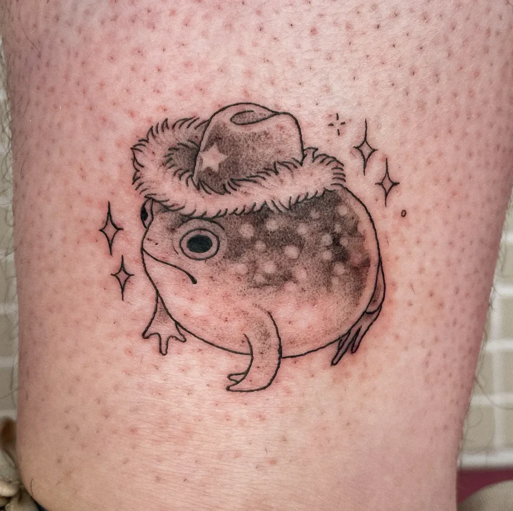 Cute toad tattoo wearing a cowboy hat with sparkles around it, playful design for animal tattoo ideas easy, arm placements, or sleeve styles.
