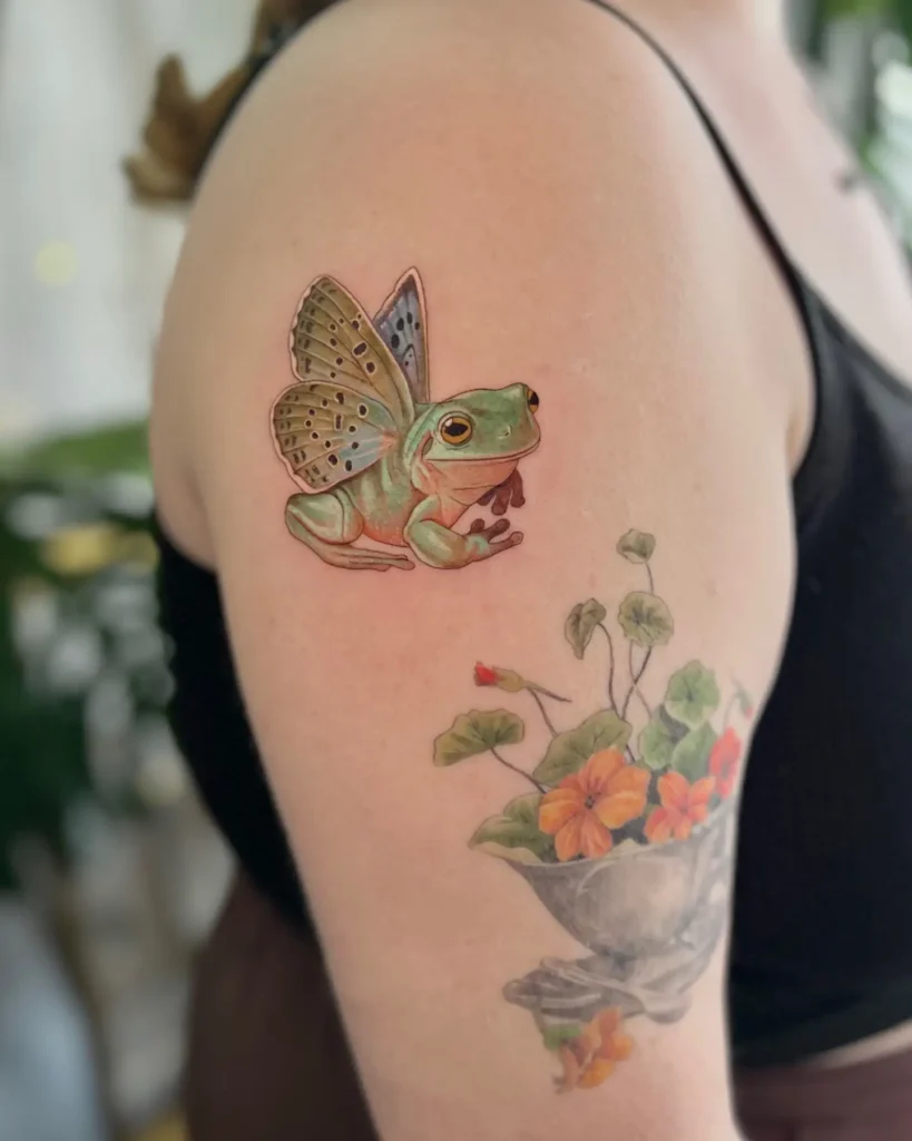 Whimsical green frog tattoo with butterfly wings on upper arm, great for animal tattoo ideas simple, arm art, or fairy-inspired sleeve designs.