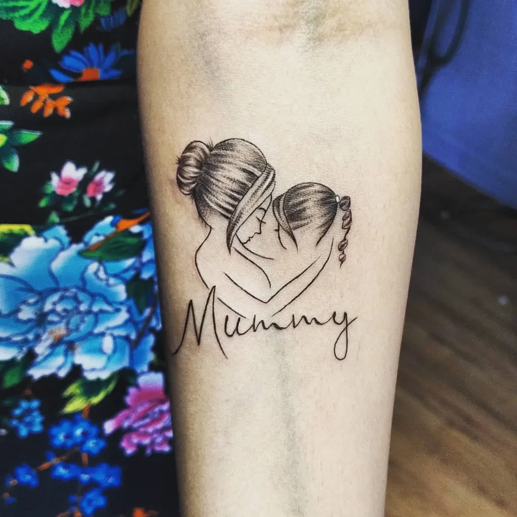 Forearm tattoo features a softly shaded drawing of a mother hugging her daughter, both with their hair tied up, faces nestled together. The word “Mummy” appears below in flowing script. The design uses black and subtle brown ink, symbolizing love, safety, and the heartfelt connection of mom and daughter tattoos.