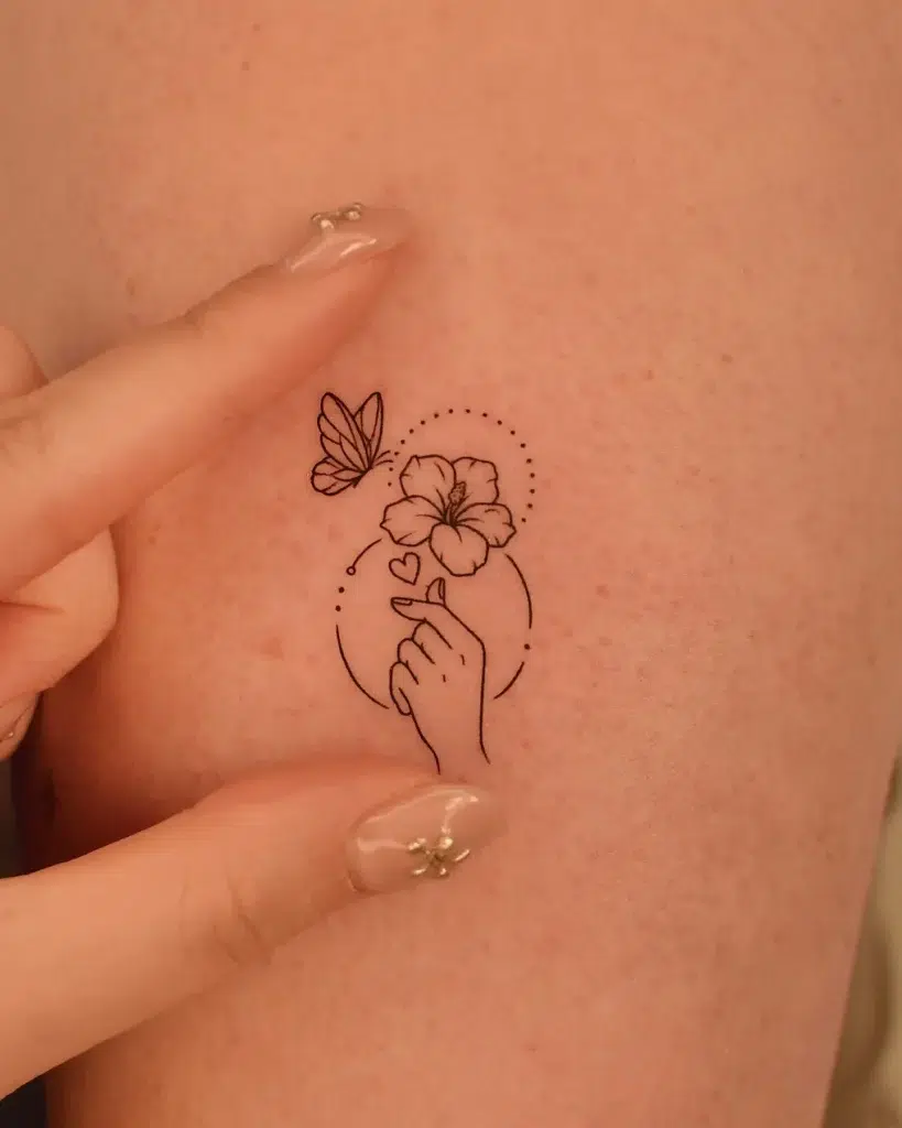 Minimal butterfly and flower tattoo featuring a hand gesture, small hearts, and a dotted circular frame. Fine-line design on soft skin, ideal for animal tattoo ideas simple and meaningful. Great for personal, small tattoo lovers looking for animal tattoo ideas easy to place with emotional symbolism and a modern minimalist feel.








