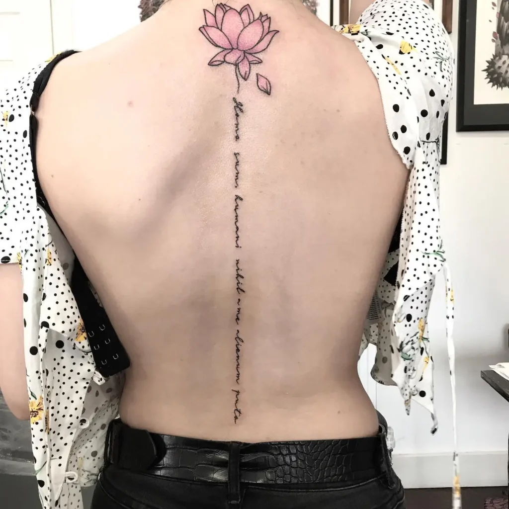 Minimalist pink lotus spine tattoo with handwritten quote, symbolizing beauty and inner strength on a woman’s back

