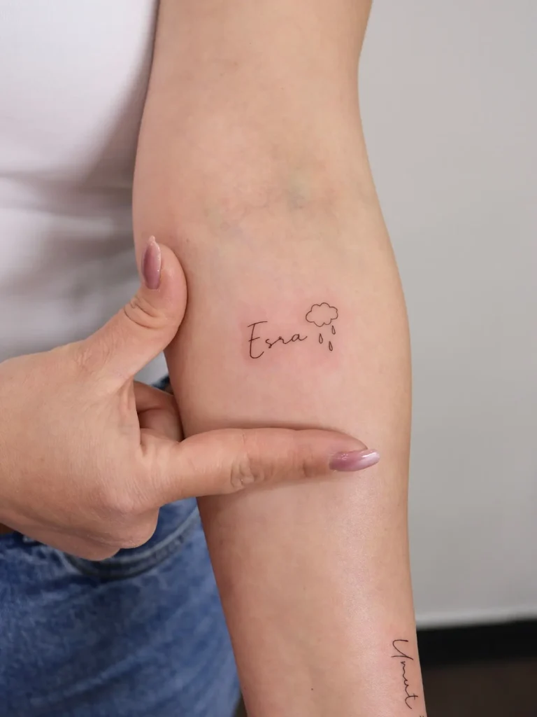 Minimalist fine line name tattoo with a small cloud and raindrops on forearm, symbolizing emotional connection, memory, and love.









