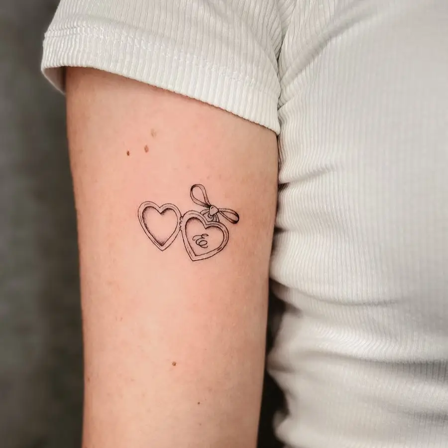 Minimal fine line tattoo of two heart lockets with a ribbon and initial, symbolizing love, memory, and personal connection.










