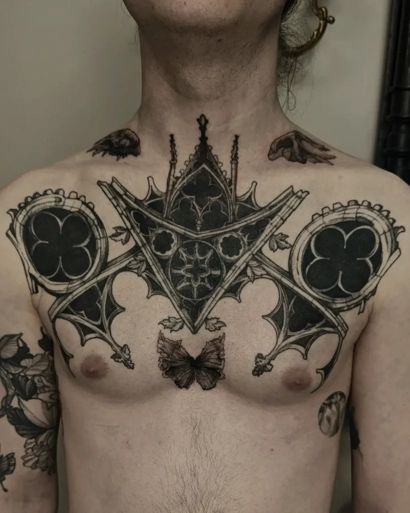 Gothic architectural chest tattoo for men with spired arches, stained glass motifs, sharp blackwork geometry, and a butterfly at the center; symmetrical and medieval in style, evoking cathedral design.